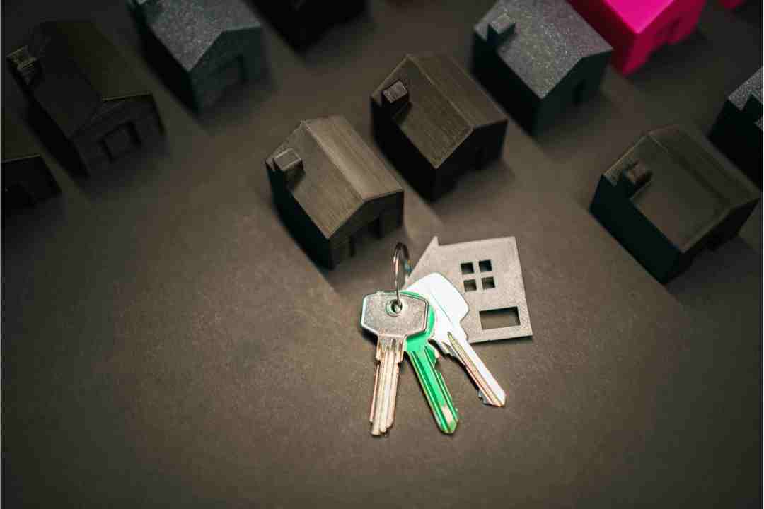 House keys and a house silhouette on a dark surface, with miniature houses in the background.
